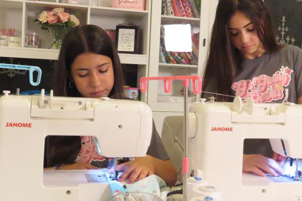 Giuliana Demma and her sister Audrina sewing pediatric hospital gowns at home for donation, inspired by a past experience of their baby cousin's ill-fitting hospital gown